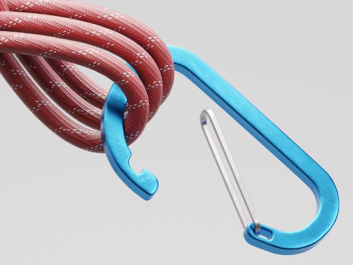 Hand holding a belay device with secondary backup knot tied below, demonstrating equipment climbing belay devices backup system