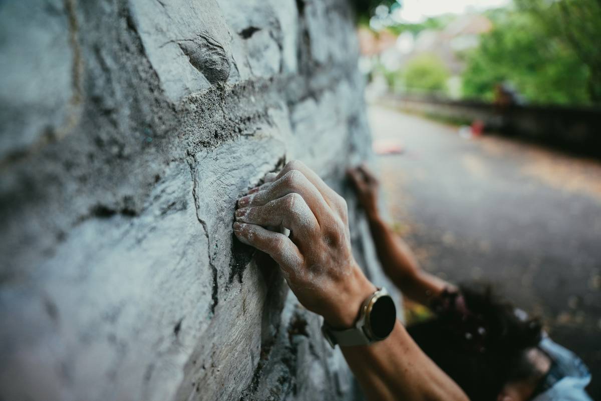 Close-up of a climber's hand gripping a belay device with rope under tension, demonstrating equipment climbing belay devices secure grip